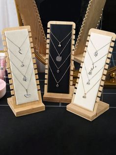 three wooden jewelry stands with necklaces and pendants on display in front of a mirror