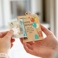 a person holding up a birthday card with balloons on it and money in the other hand