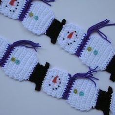 crocheted snowmen are lined up on a white surface with purple and black ribbons