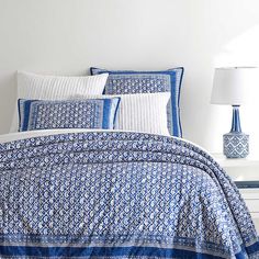 a bed with blue and white comforters on top of it next to a night stand