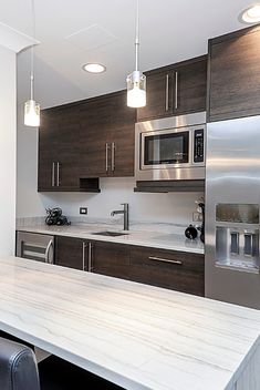 a modern kitchen with stainless steel appliances and marble counter tops, along with dark wood cabinets