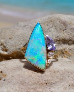 Large Asymmetrical Aqua/Rainbow Australian Opal Statement Ring paired with Cornflower Blue Spinel and Diamond Accents in Solid 14k Yellow Gold. 23mm in length and 14mm wide. This captivating Australian Opal Ring exudes a cosmic allure reminiscent of the tranquil waters of the Maldives. Functioning as a talisman to activate the throat chakra, it promotes clear and unrestrained communication while harmonizing with the energies of the third eye and crown chakras, nurturing inspired and intuitive wi Unique Blue Multi-stone Opal Ring, Fine Blue Opal Multi-stone Ring, Blue Multi-stone Opal Ring Fine Jewelry, Fine Jewelry Multicolor Multi-stone Opal Ring, Blue Multi-stone Opal Ring In Fine Jewelry Style, Blue Opal Multi-stone Jewelry, Opal Statement Ring, Lavender Opal, Australian Opal Ring