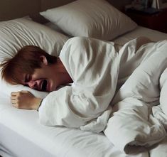 a woman is laying in bed with her head on the pillow and mouth wide open