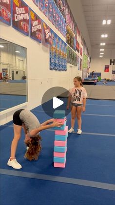 two girls are playing with blocks on the floor in an indoor gym area, while one girl is doing a handstand