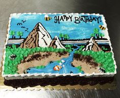 a birthday cake is decorated with an image of a river and mountains in the background