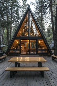 a - frame cabin in the woods with picnic tables and benches on the front deck