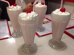 three milkshakes with cherries and whipped cream on top sit on a table