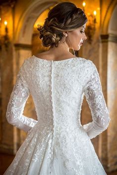 a woman in a white wedding dress with long sleeves and an intricate lace pattern on the back