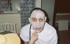 a man with white paint on his face and wearing a towel around his neck is looking at the camera