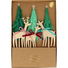 three wooden reindeer ornaments in a cardboard box with ribbon and bows on the front, two are green and one is white