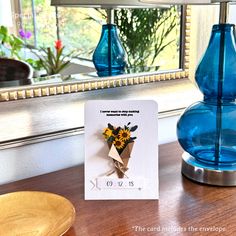 a blue vase sitting on top of a table next to a card with flowers in it