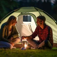 a man and woman sitting in front of a tent with a lantern on the ground