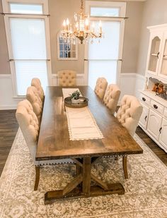 a dining room table with beige chairs and a chandelier hanging from the ceiling