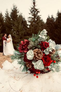 a bride and groom are standing in the snow with pine cones on their bouquets