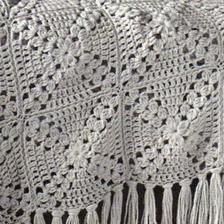 a white crocheted blanket with tassels on it