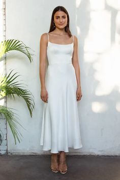 a woman standing in front of a wall wearing a white dress