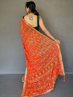 Look stunning in this classic orange printed georgette festival wear saree with a blouse! The saree is 5.50 meters long and made of high-quality georgette material with bandhani print all over, and gotta pati lace border with tassels work. The green blouse in georgette material with a gotta patti lace border adds a beautiful contrast to the saree. The saree is perfect for weddings, festivals, events, or even casual wear. It's customizable and comes with an stitched 1.00 meters blouse. Festive Saree, Bandhani Print, Georgette Material, Color Plain, Pretty Orange, Gotta Patti, Print Saree, Readymade Saree, Plain Blouse