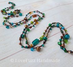 a long necklace with multicolored beads on a white wooden surface and the words love fizz handmade written below it