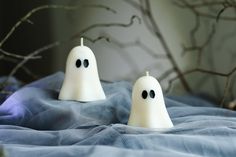 two white ghost candles sitting on top of a bed