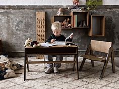 a little boy sitting at a desk with a book and stuffed animals in the background