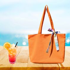 an orange tote bag sitting on top of a wooden table next to a drink