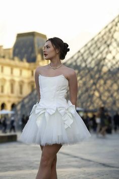 This ivory-colored dress features a bodice in the form of a corset, adorned with a voluminous skirt embellished with decorative bows. The corset serves as the upper part of the dress, providing a form-fitting and structured appearance to the ensemble. The ivory hue of the dress imparts an elegant and timeless quality. The skirt, characterized by its generous volume, adds a touch of sophistication to the overall design. The use of decorative bows enhances the visual appeal of the dress, creating 2 Piece Homecoming Dress, Strapless Homecoming Dresses, White Tulle Dress, White Homecoming Dresses, Lace Formal Dress, Satin Short, Lace Homecoming Dresses, Short Homecoming Dress, White Tulle