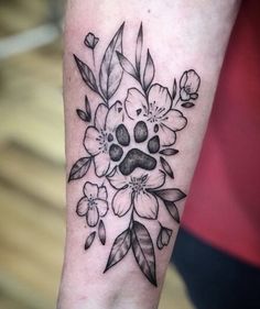 a black and white flower tattoo on the left arm, with an image of a dog's paw surrounded by flowers