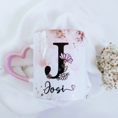 a pink and white coffee mug with the letter j on it next to some dried flowers