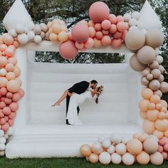 a couple kissing in front of an inflatable arch made out of balloons on the lawn