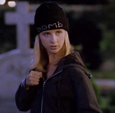 a woman wearing a black hat and jacket standing in front of a gravestone at night