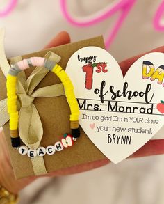 a hand holding a heart shaped card with two bracelets on it and a teacher's day tag