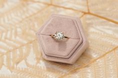 an engagement ring sitting on top of a pink velvet box with a diamond in it