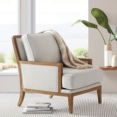 a chair with a blanket on it in front of a window next to a potted plant