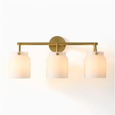 three light bathroom fixture in brass finish with white glass shades on the bottom and sides