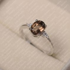 an engagement ring with a large brown stone and two white diamonds on the side, in a box