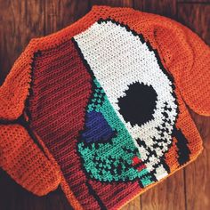 an orange knitted sweater with a skull on the front and back, sitting on top of a wooden floor