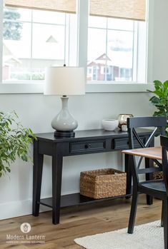 a table with a lamp and some plants on it in front of a large window