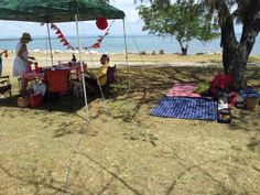 some people are sitting at a picnic table under a green tent near the water and trees