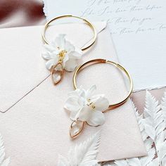 two white flowers sitting on top of a piece of paper next to a pair of gold hoop earrings