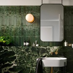 a bathroom with green marble walls and flooring, a round mirror above the sink