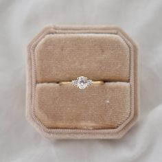 an engagement ring in a velvet box on a white cloth covered surface with a gold band