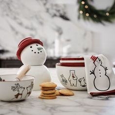 a snowman made out of cookie cookies next to some bowls and mugs on a counter