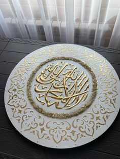 a white and gold plate with arabic writing on the surface next to a window sill