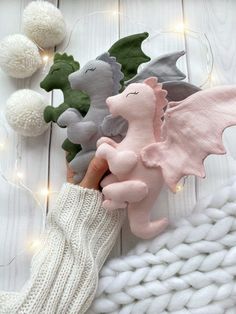 a hand is holding some stuffed animals on a white blanket with lights in the background