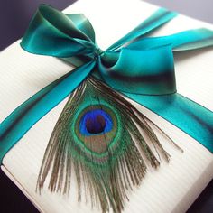 a peacock feather wrapped in satin ribbon on a white gift box with a green bow