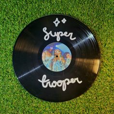 a vinyl record with the words super troopers written on it in white ink and surrounded by green grass