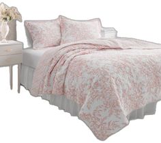 a bed with pink and white bedspread on it next to a night stand