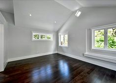 an empty room with hardwood floors and three windows