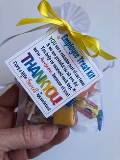 a hand holding a candy bag with thank you notes on it and a yellow ribbon