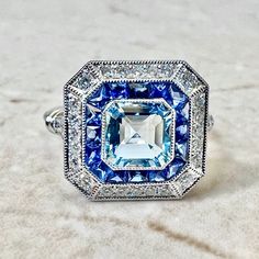 Breathtaking handcrafted platinum Art Deco style aquamarine, sapphire and diamond ring! The center stone is a lovely 1.05 carat aquamarine. It is surrounded by a row of fine French cut sapphires weighing 0.70 carat. The sapphires are haloed by 0.40 carat of round diamonds. Fine milgrain adds to the delicacy of the ring. Beautiful openwork filigree decorate the under gallery. The ring measures 13.97 x 13.63 mm from side to side. Stamped Pt900. Ring size 6.25-6.5 US / M-M 1/2 UK. > Resizing includ Blue Octagon Sapphire Ring With Diamonds, Blue Art Deco Diamond Ring With Center Stone, Art Deco Blue Diamond Ring With Center Stone, Blue Octagon Diamond Ring, Gia Certified Blue Topaz Ring With Diamond, Gia Certified Blue Topaz Diamond Ring, Blue Octagon Brilliant Cut Sapphire Ring, Blue Octagon Sapphire Ring With Brilliant Cut, Octagon Shaped Blue Sapphire Ring With Brilliant Cut